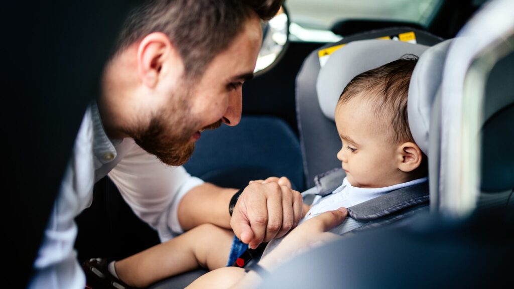 A father leaning over his toddler son in a car seat, representing the conversation about empathy and the beggar at the red light.
